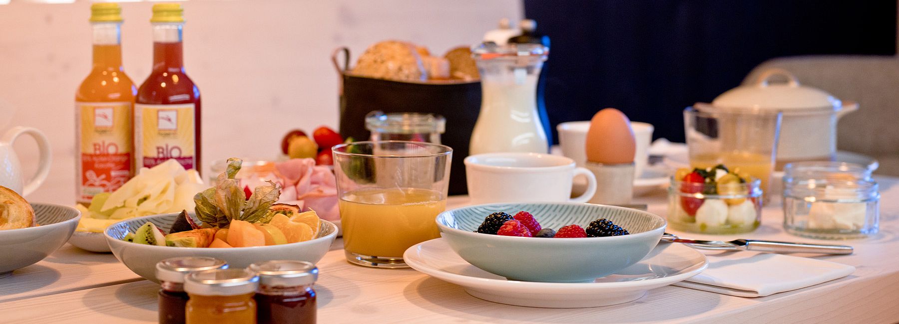 Reich gedeckter Frühstückstisch mit Saft, Obst, Eiern und Käse