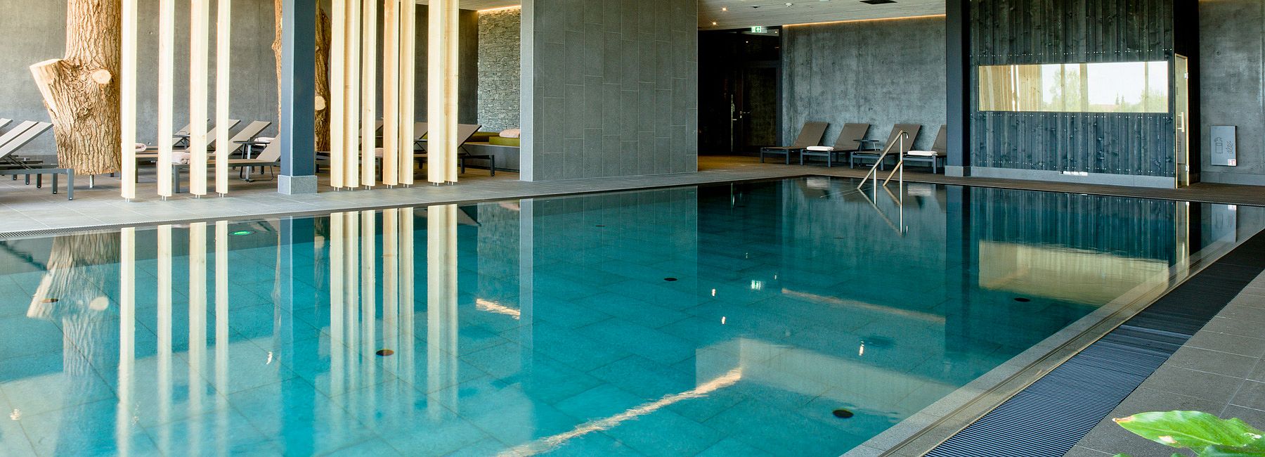 Wellnessbereich mit großem Indoorpool und Ruhebereich mit Liegen und Trennelementen aus Holz