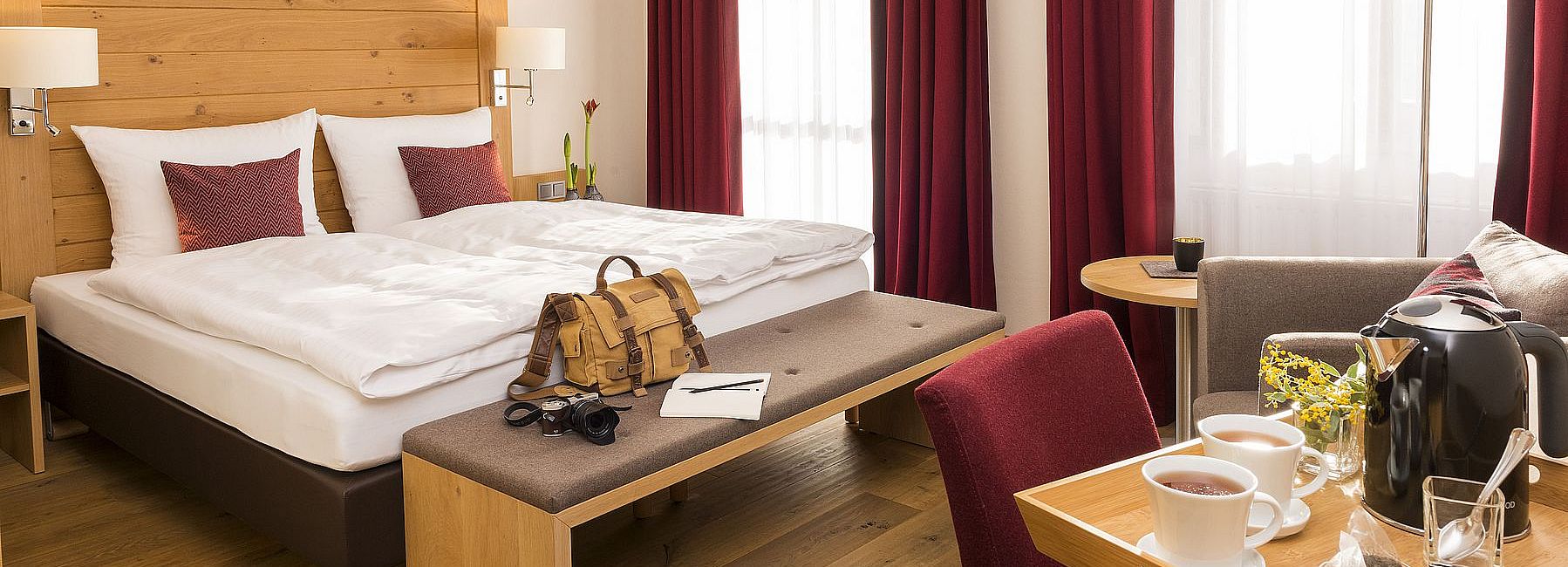 Helles Hotelzimmer mit moderner Einrichtung, Doppelbett, Loungesessel und Teebar