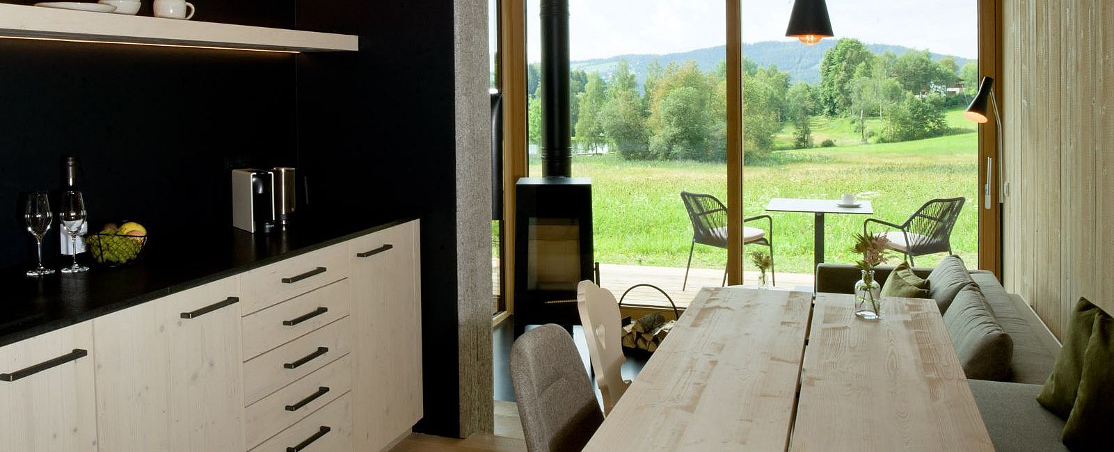 Offene Wohnküche und Sitzecke mit Kamin und Blick auf die Wiese vor dem Chalet