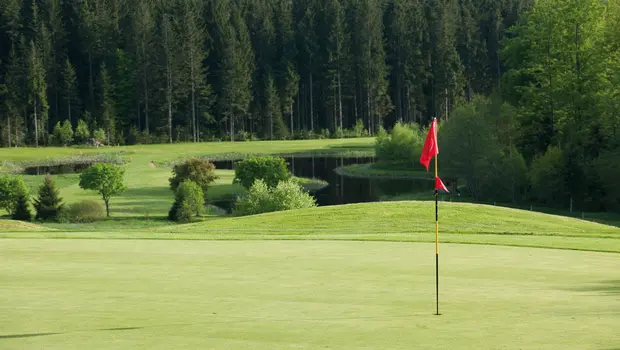 Golfgrün mit roter Fahne und Wasserhindernis auf einem Golfplatz im Bayerischen Wald