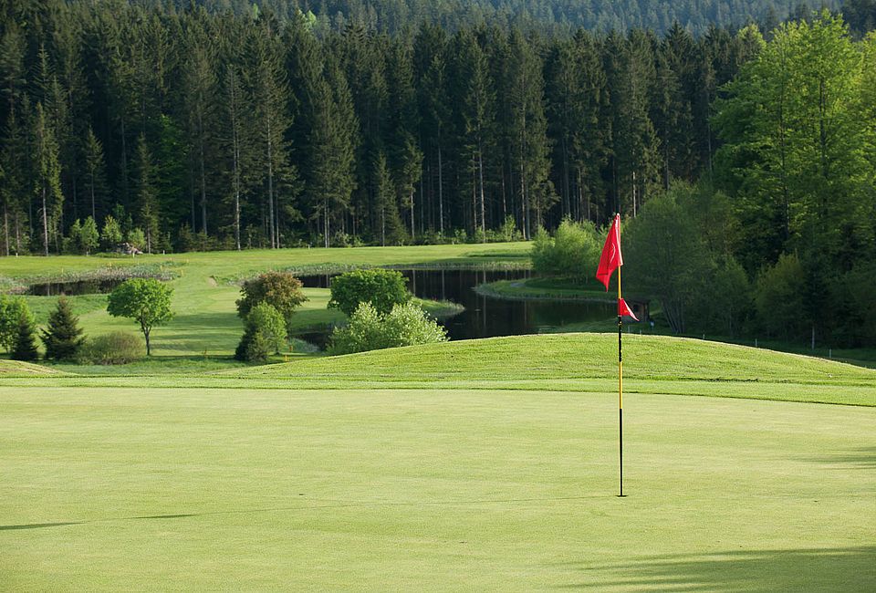 Golfgrün mit roter Fahne und Wasserhindernis auf einem Golfplatz im Bayerischen Wald