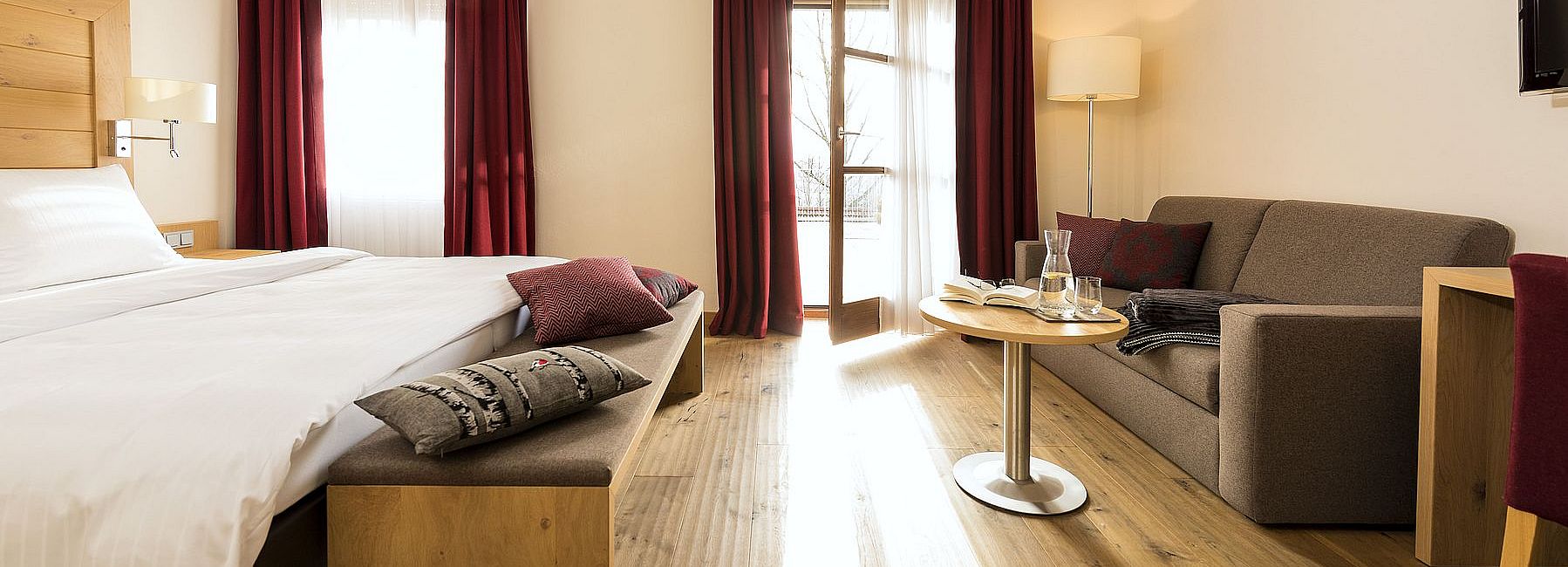 Helles Hotelzimmer mit moderner Einrichtung, Doppelbett und gemütlichem Sofa und Balkon