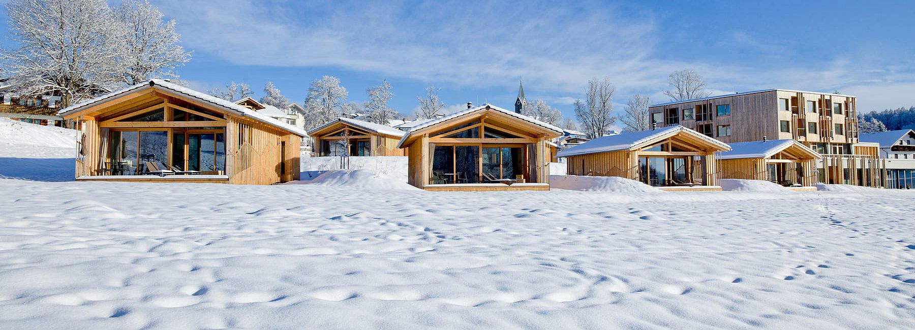 Mehrere Chalets in winterlicher Schneelandschaft unter blauem Himmel