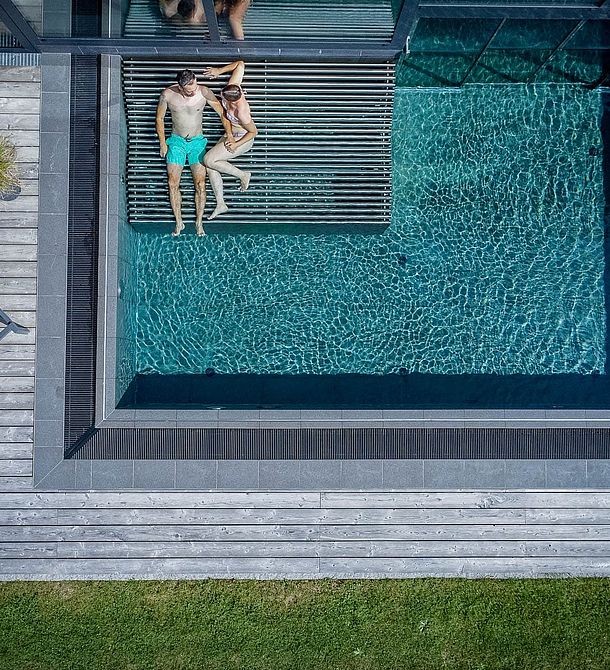 Drohnenaufnahme eines Paares auf der Sitzbank im Außenpool