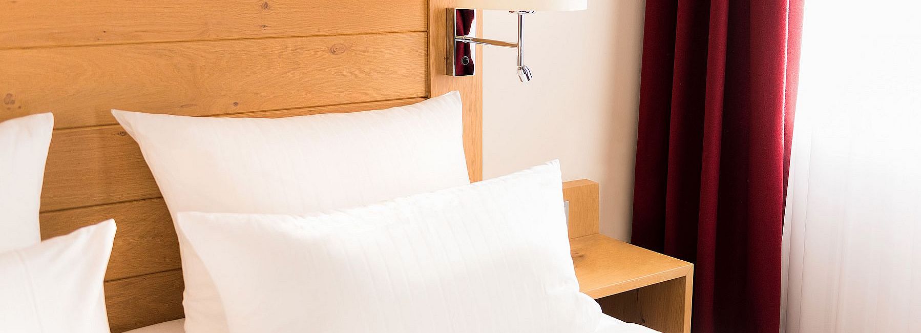 Doppelbett in einem Hotelzimmer mit hölzernem Kopfteil und roten Vorhängen