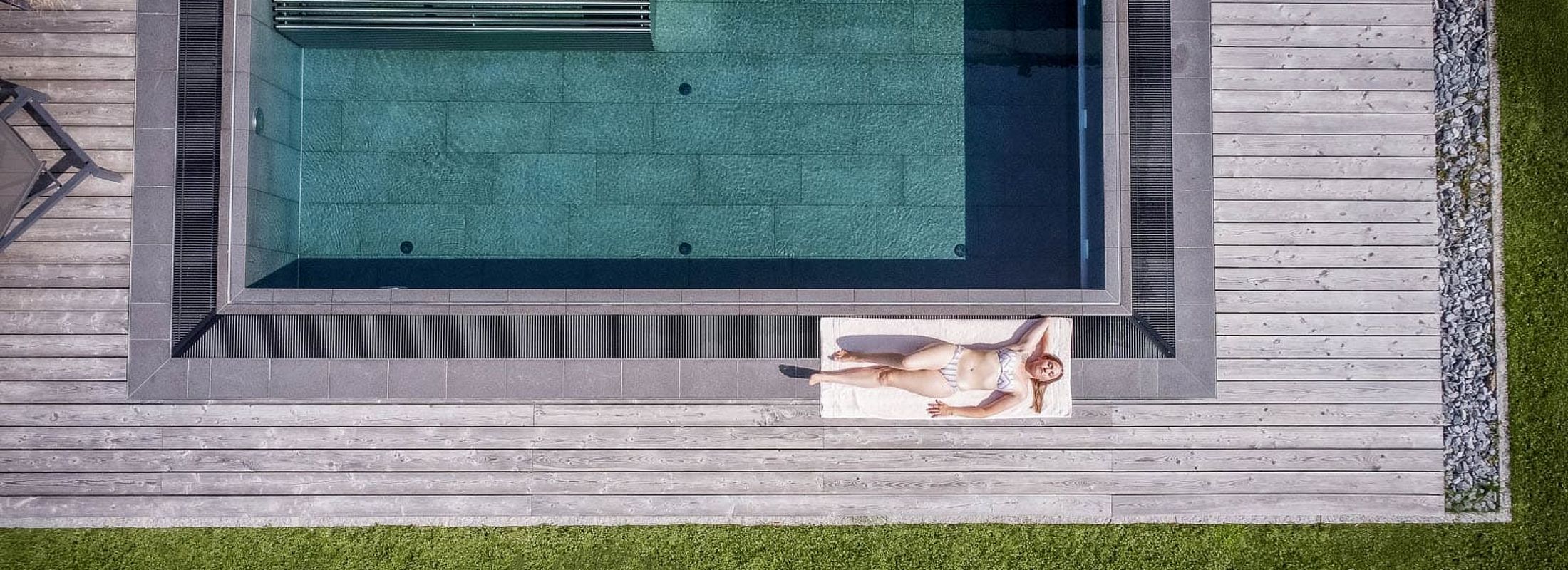 Drone view of an infinity pool with wooden deck and relaxation area at the nature hotel