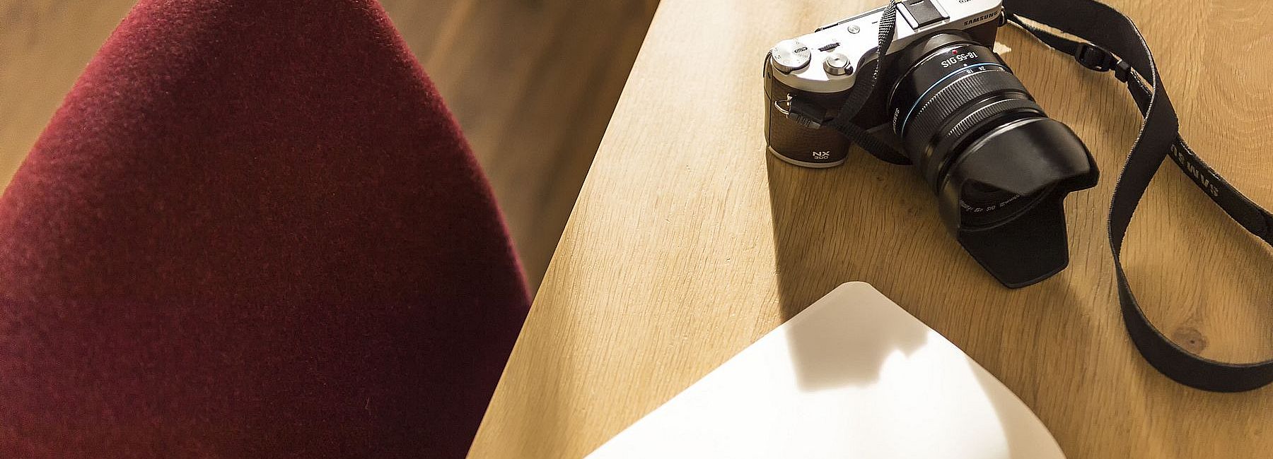 Kamera, Notizblock und Stift auf einem Schreibtisch mit rotem Schreibtischsessel