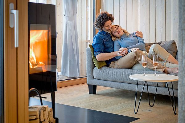 Paar kuschelt auf Sofa vor Kamin mit zwei Gläsern Roséwein auf dem Tisch
