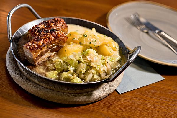 Schweinekrustenbraten in einer Pfanne mit frischen Kartoffeln und Kraut
