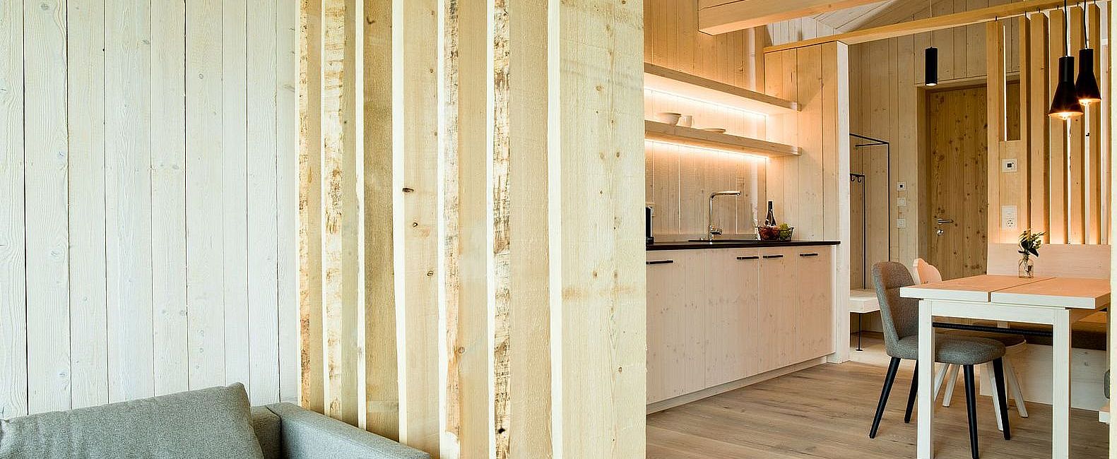 Chalet mit Wohnküche aus Holz, Esstisch mit stimmungsvoller Beleuchtung und Wohnecke mit Sofa