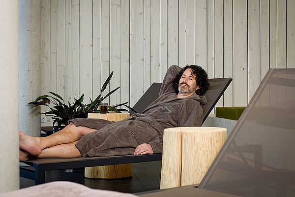 Mann entspannt sich im Bademantel auf einer Liege im Wellnessbereich