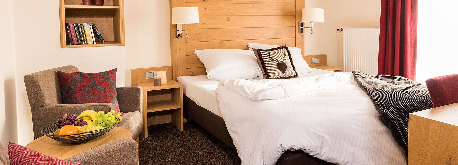Hotelzimmer mit Bett, rotem Dekokissen und Obstschale im gemütlichen Sitzbereich