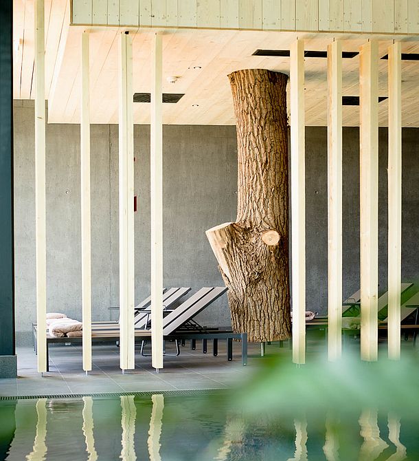 Ruhebereich im Spa mit Liegen, Holzsäulen und Baumstamm-Design neben dem Innenpool