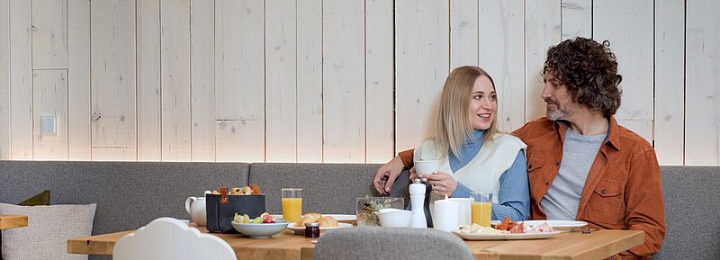 Paar beim Frühstück mit frischem Brot, Wurst, Käse und Orangensaft