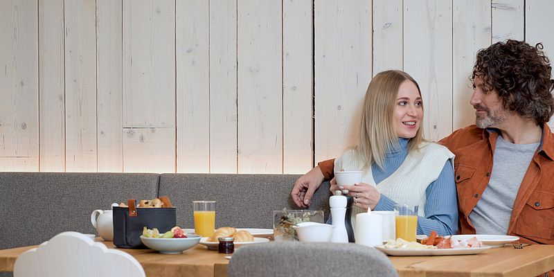 Paar beim Frühstück mit frischem Brot, Wurst, Käse und Orangensaft