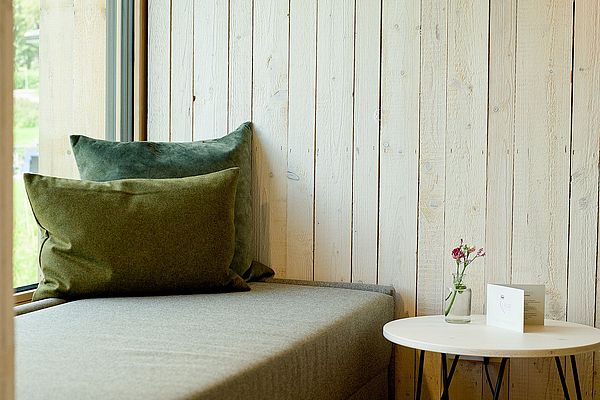 Gemütlicher Fenstersitz mit grünen Kissen und Beistelltisch vor rustikaler Holzwand