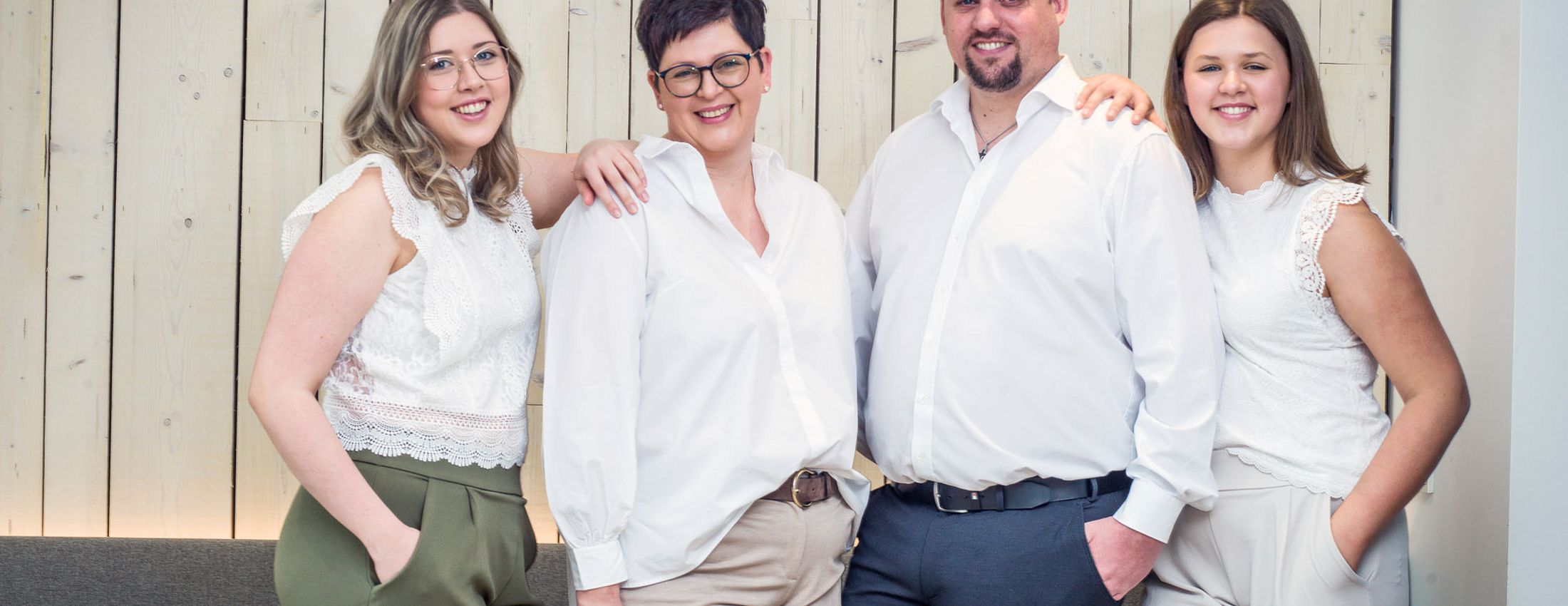 Familie und Gastgeberteam des Hotels vor heller Holzwand im Innenbereich