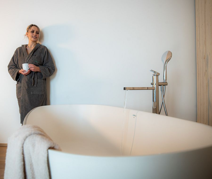 Woman in bathrobe standing next to freestanding bathtub