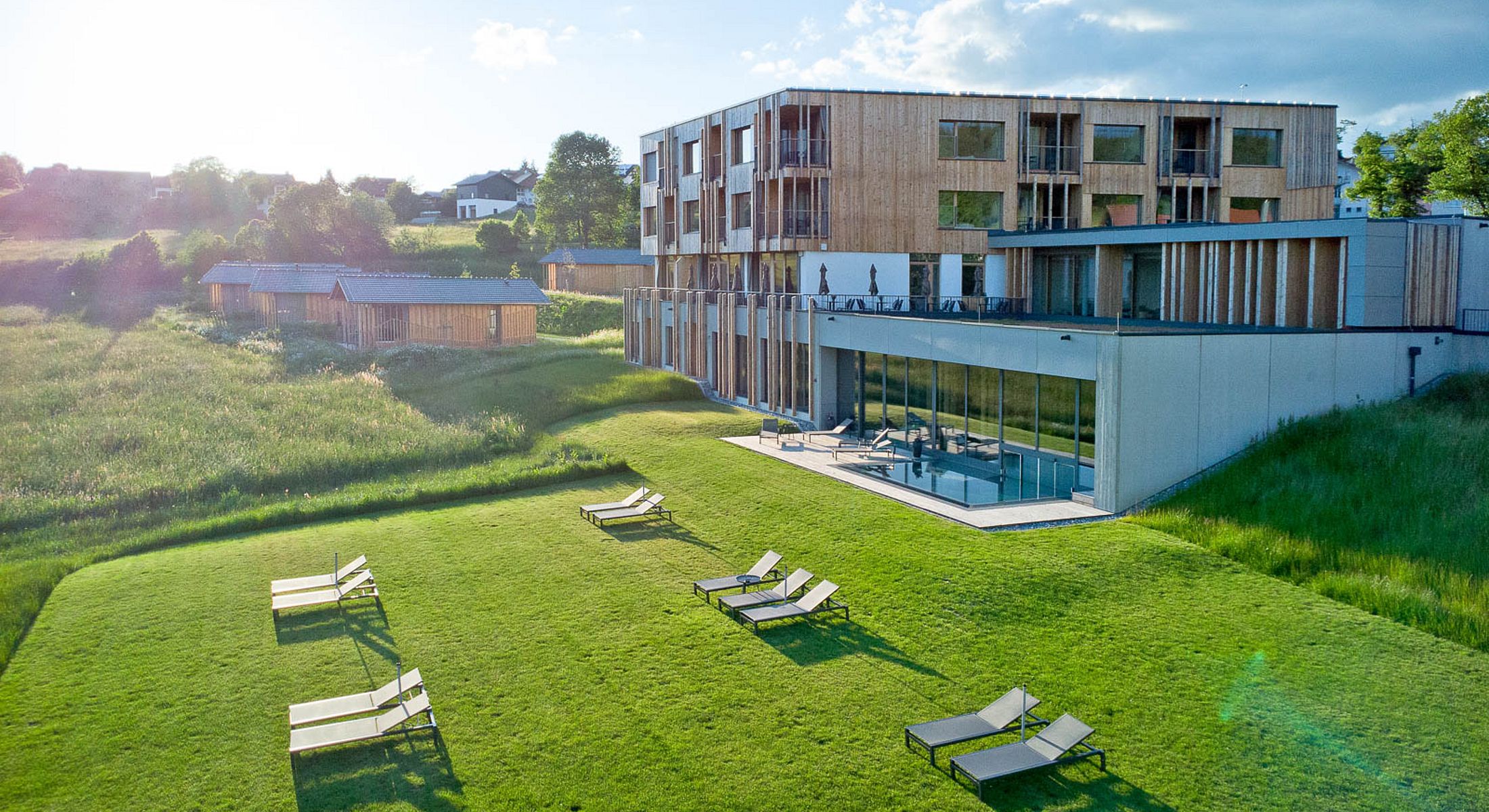 Hotelanlage mit Liegewiese und Poolbereich vor moderner Holzarchitektur