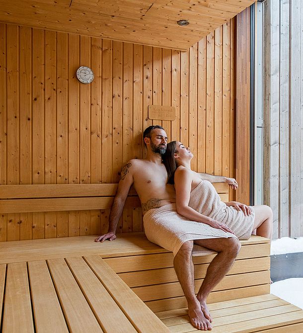 Paar entspannt in der Sauna mit Handtüchern und Blick nach draußen