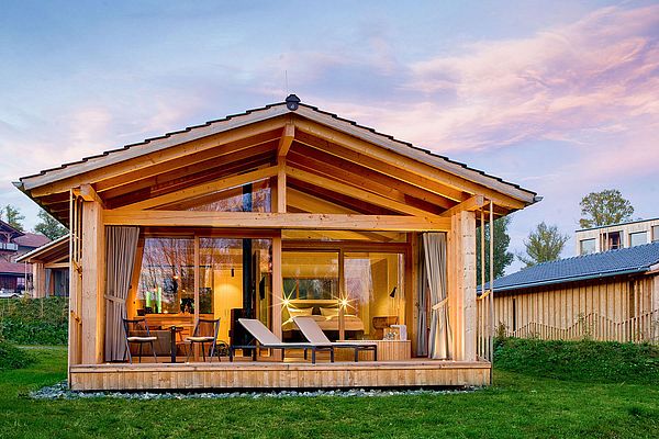 Frontansicht des beleuchteten Chalets bei Sonnenuntergang mit Glasfront