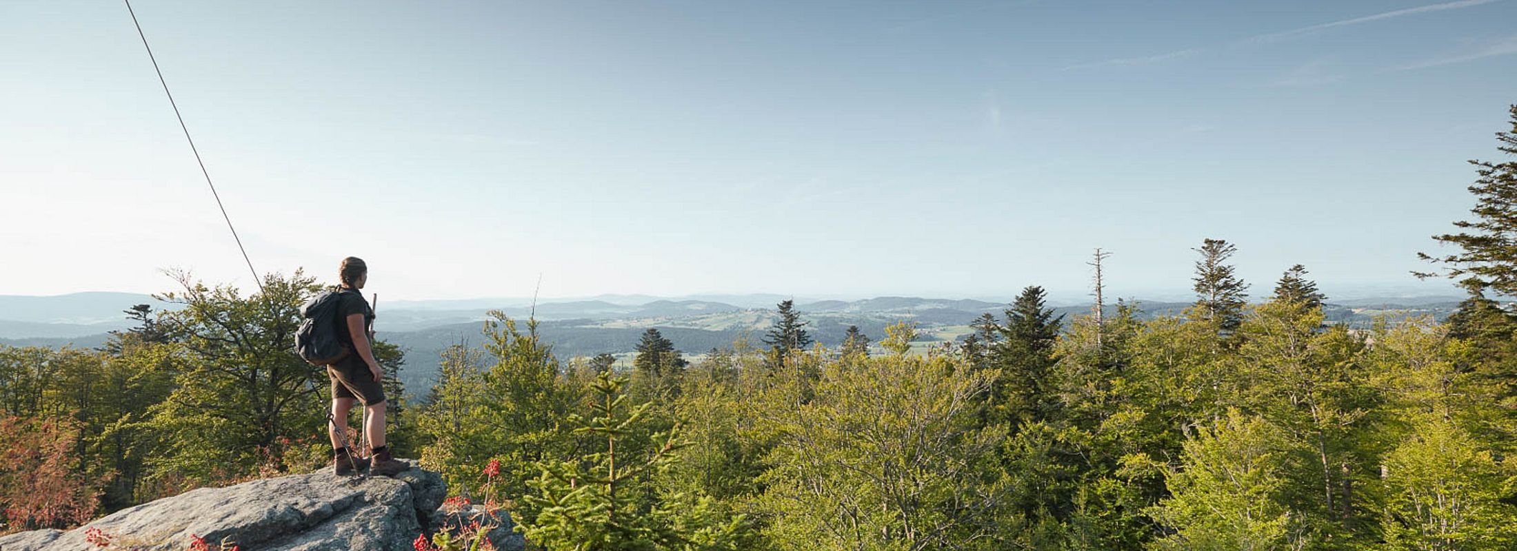Wanderer auf Felsen mit weitem Panoramablick über die Landschaft des Bayerischen Waldes