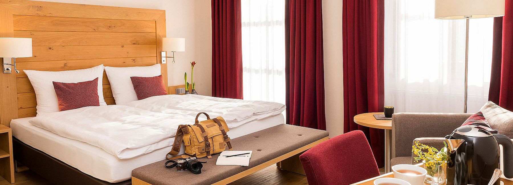 Helles Hotelzimmer mit moderner Einrichtung, Doppelbett, Loungesessel und Teebar