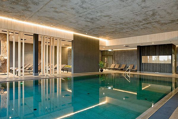 Wellnessbereich mit großem Indoorpool und Ruhebereich mit Liegen und Trennelementen aus Holz