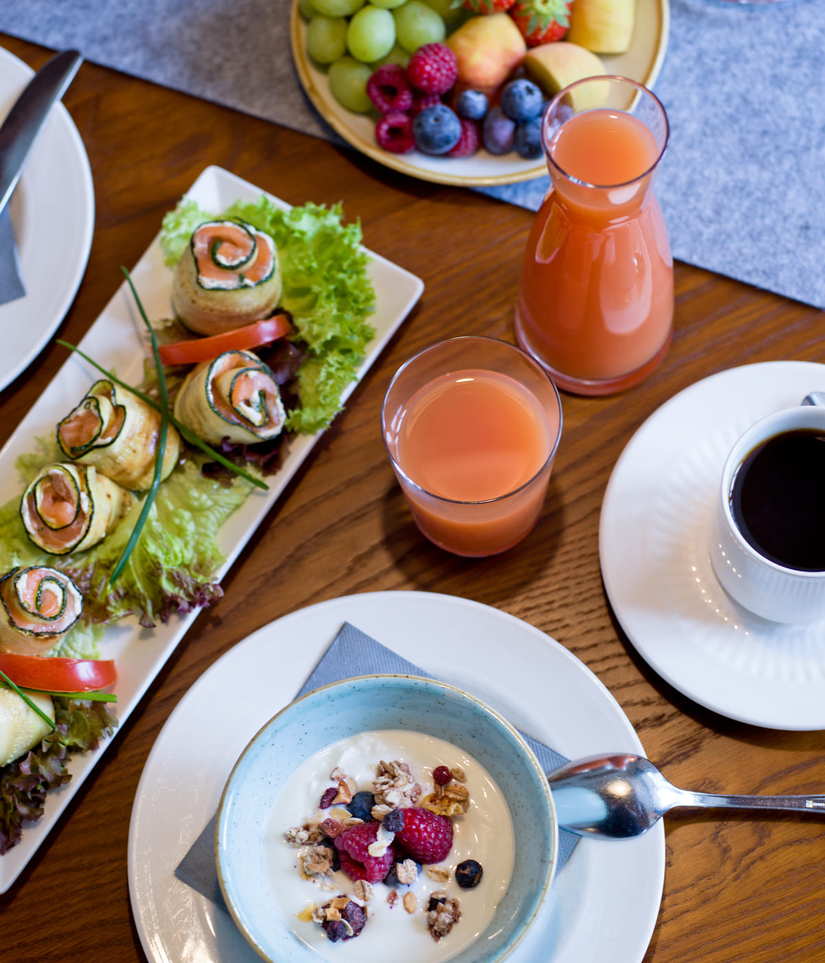 Frühstückstisch mit frischem Obst, Joghurt mit Beeren, Saft und Kaffee auf Holzplatte